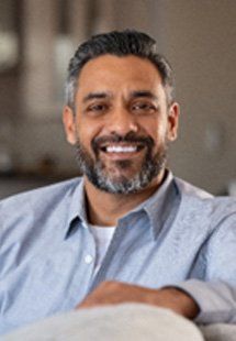 Mature man in blue shirt smiling while relaxing on couch