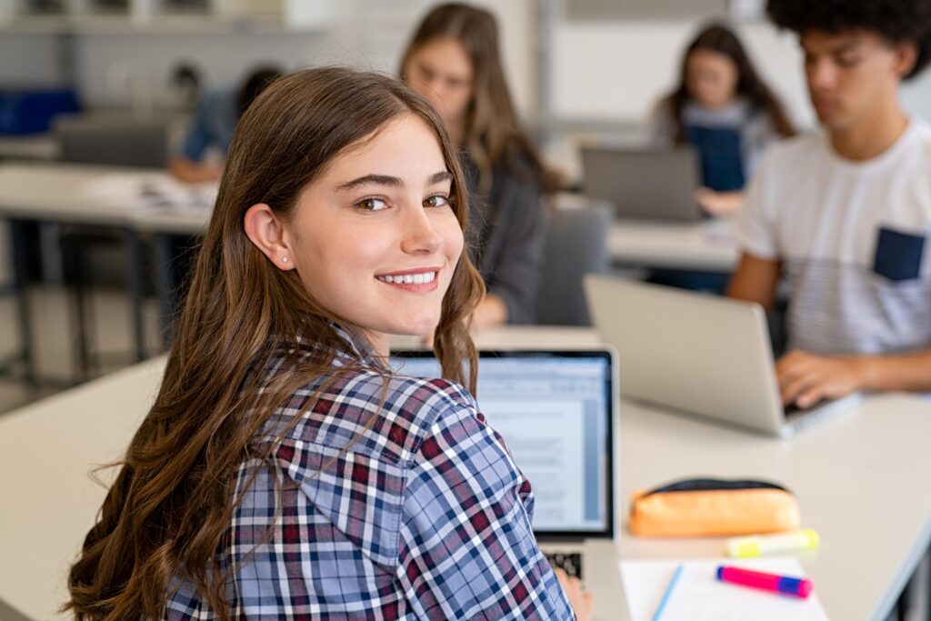 Teen smiling while working on laptop in classroom