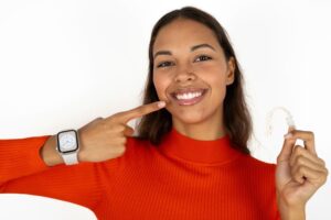 Young woman pointing at her teeth, holding SureSmile aligner